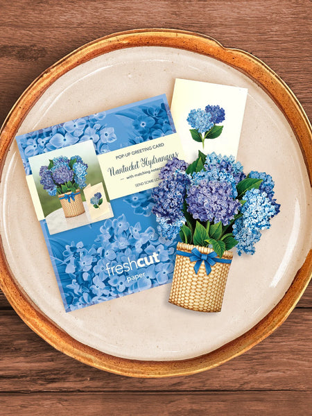 Mailing envelope, notecard and Mini Hydrangea greeting card laid out on charger on table
