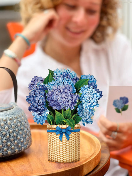 woman reads notecard as Mini Nantucket Hydrangeas greeting card sits, pop-up on table beside her