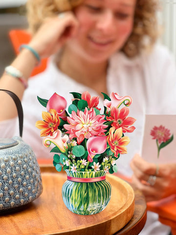 Woman reads notecard in background and Mini Dear Dahlia greeting card sits on table next to a teapot in foreground