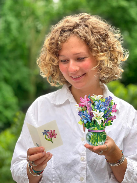 Model holds Mini Lilies & Lupines greeting card in one hand and reads notecard, held in the other hand