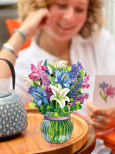 Model sits by table reading notecard and Lilies & Lupines greeting card sits on table next to teapot