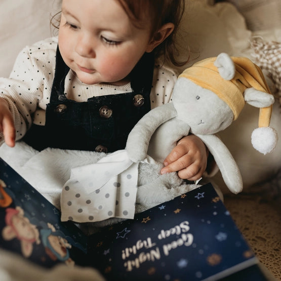 Toddler holds plush Sleepy Bloom Bunny and Good Night, Sleep Tight book 