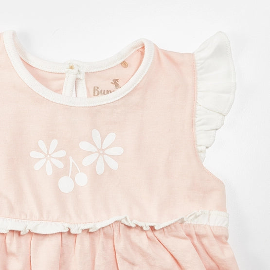 Close up view of pink bubble romper with ruffle sleeves and bodice, white flowers